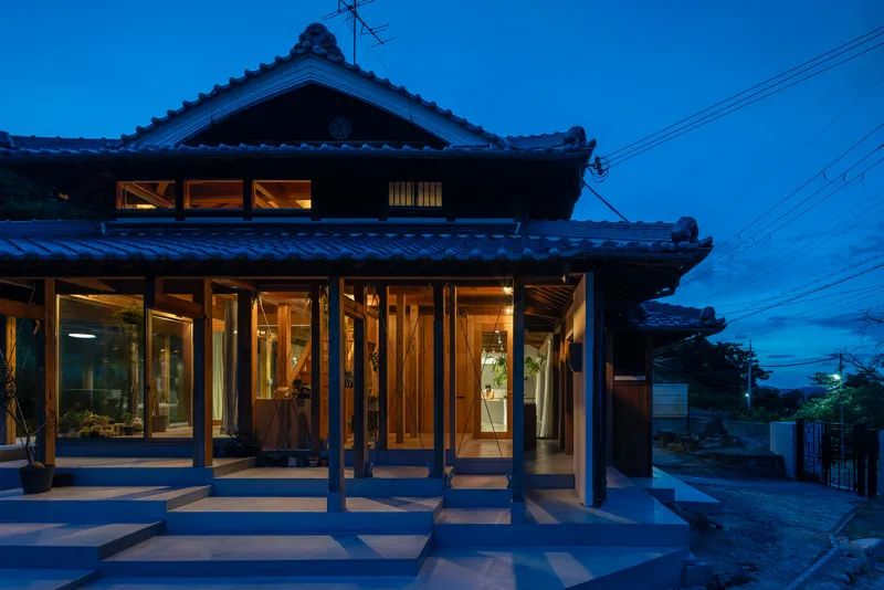 Glass-walled veranda with timber posts under traditional tile roof illuminated at twilight