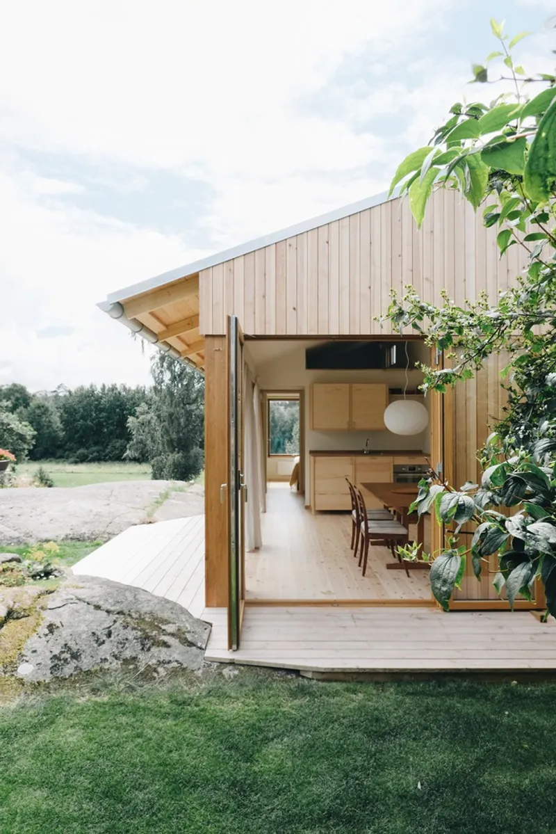 Open timber-clad pavilion with bifold doors leading to a dining area framed by greenery and open field