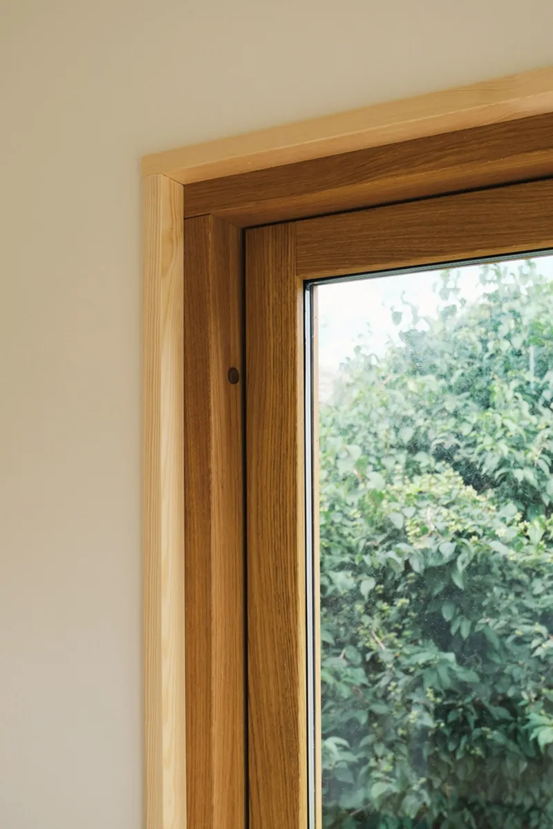 Close-up of window frame detail showing timber jamb and transom meeting pale plaster wall