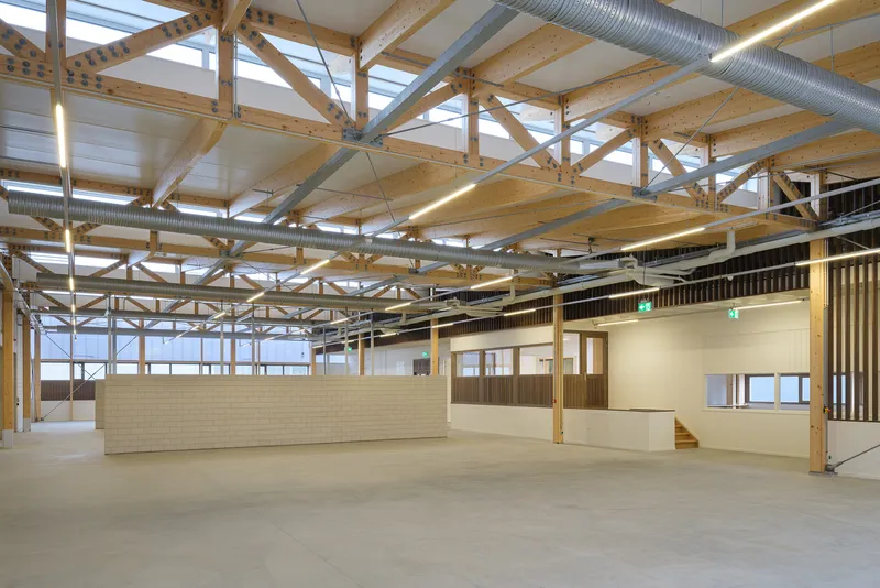 Main hall interior: glulam timber trusses, steel cross-bracing, and open floor with supervision rooms behind