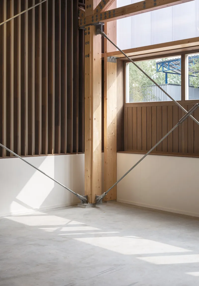 Interior detail: timber column, steel cross-brace, and polycarbonate wall admitting diffused daylight