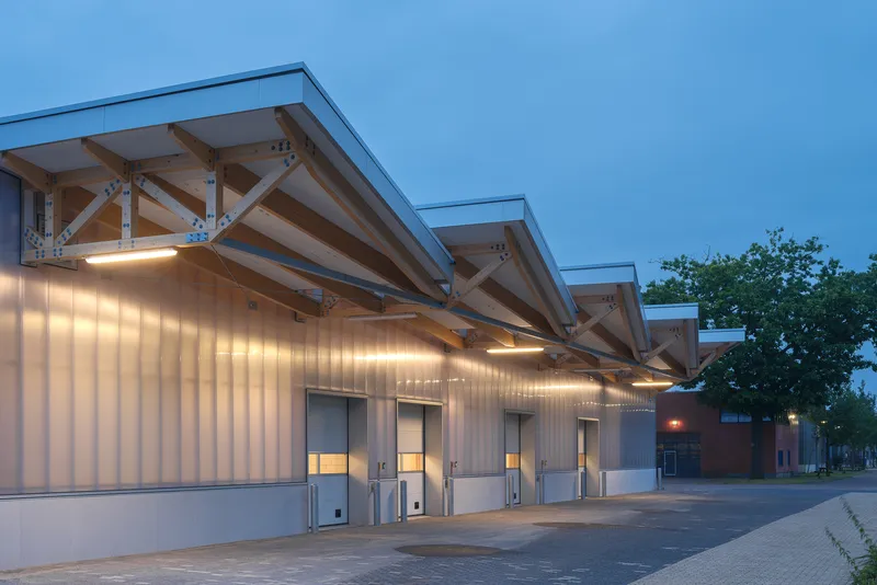 Expedition canopy at dusk: perspective along the loading dock with exposed timber structure overhead