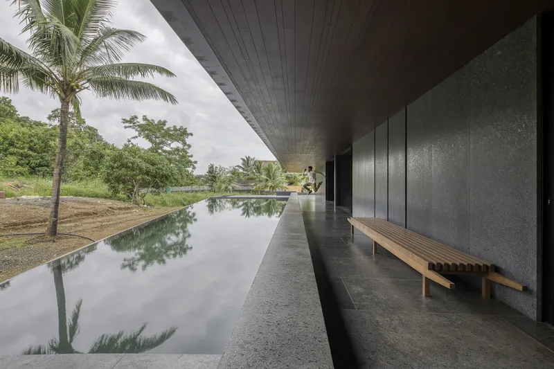 Covered walkway alongside reflecting pool with timber bench against textured concrete wall