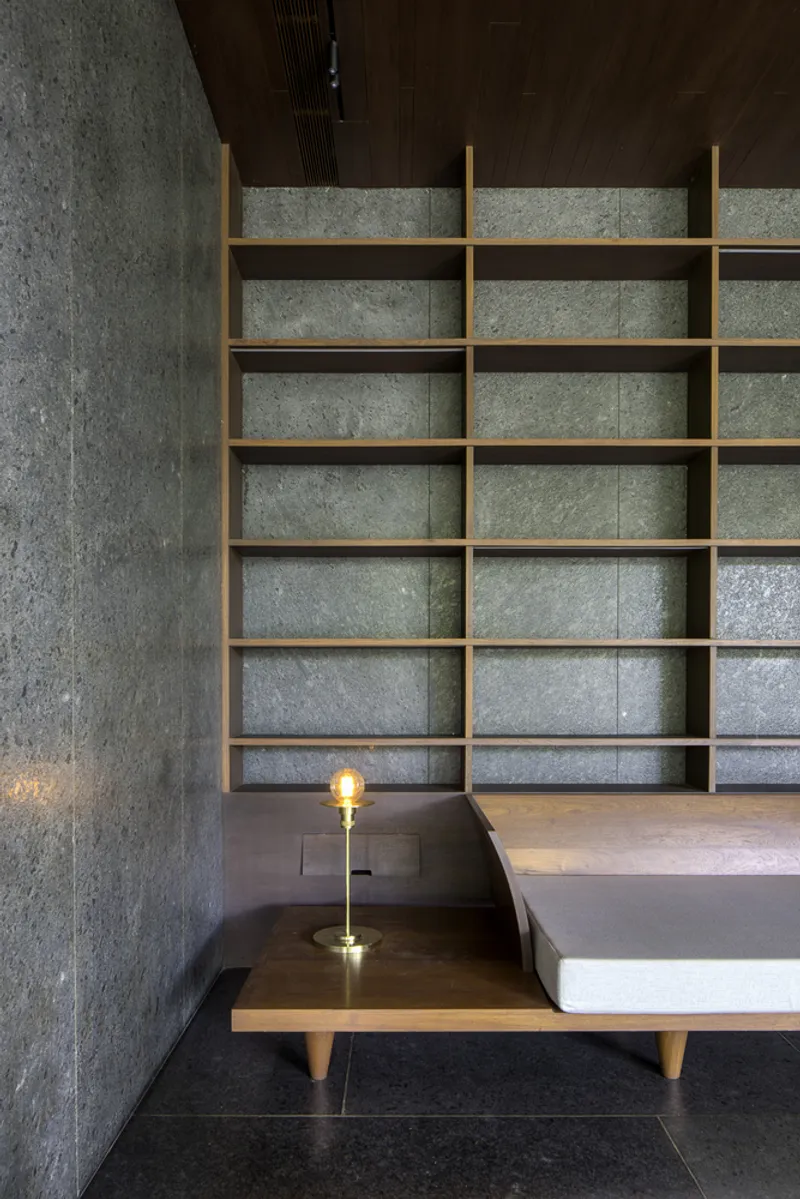Built-in timber shelving unit against textured concrete wall with low platform seating and table lamp