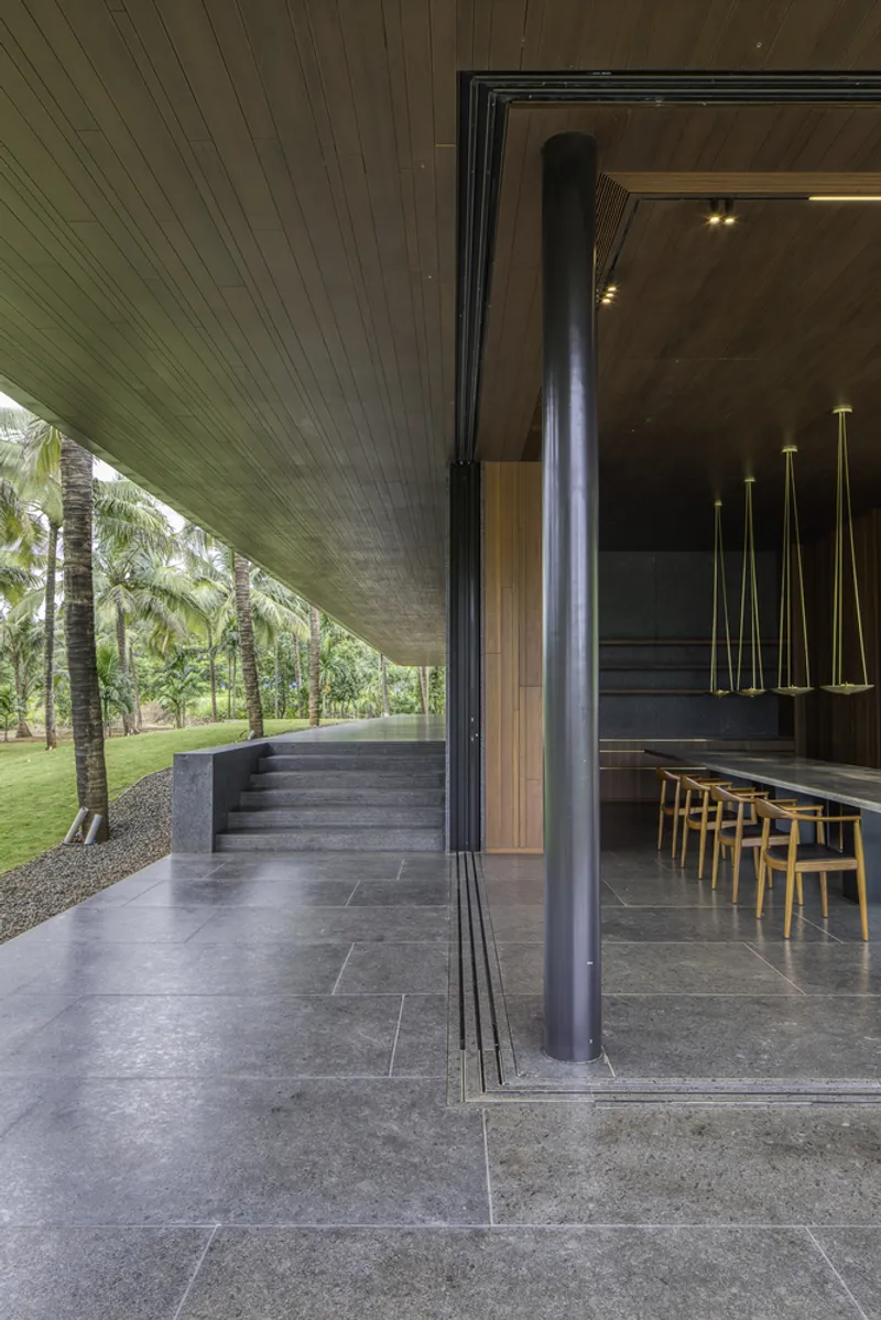 Covered terrace with timber slat ceiling and steel column looking toward interior dining space with suspended pendants