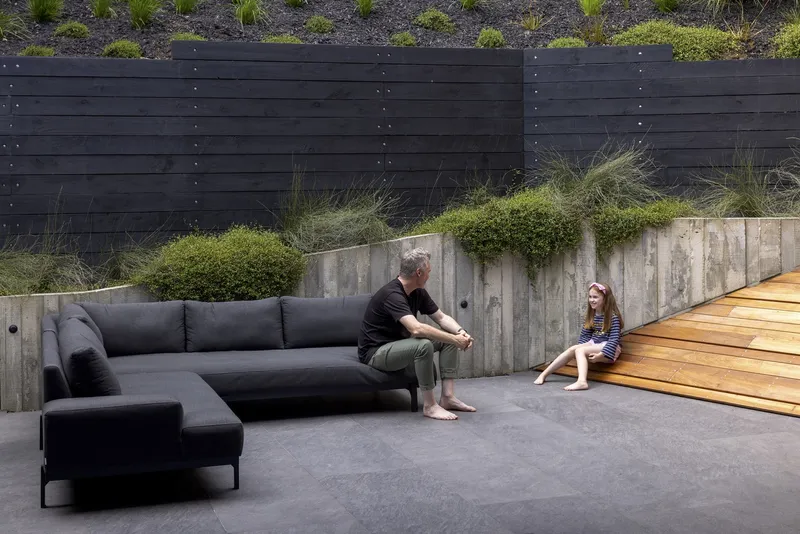 Sunken courtyard with board-formed concrete retaining walls, planted beds, and two figures seated