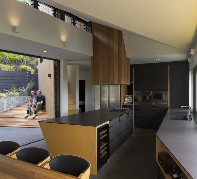 Kitchen with timber-clad island and rangehood looking through to deck where two figures sit