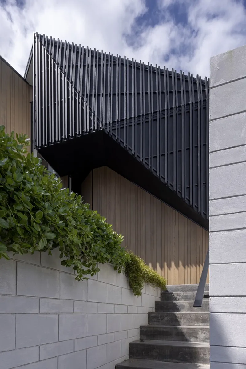 Cantilevered black vertical screen box above a concrete retaining wall with planted greenery