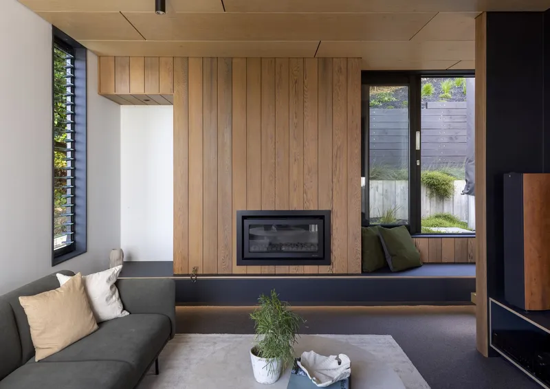 Living room with timber wall concealing a fireplace and built-in window seat with courtyard view