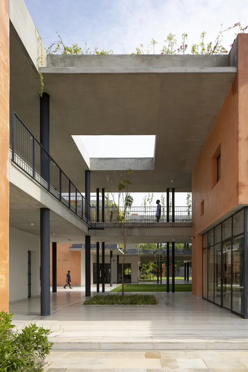 Courtyard view of stacked concrete volumes with central planted beds and rooftop greenery under blue sky