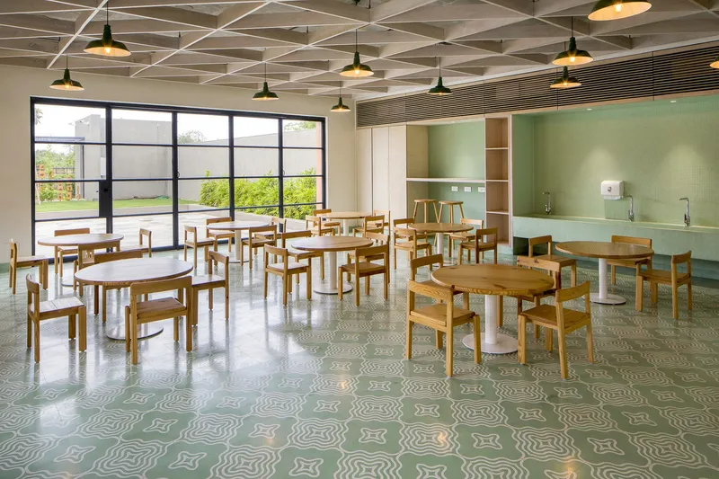 Dining hall with patterned terrazzo floor, wooden tables and pendant lights hung from exposed ceiling grid