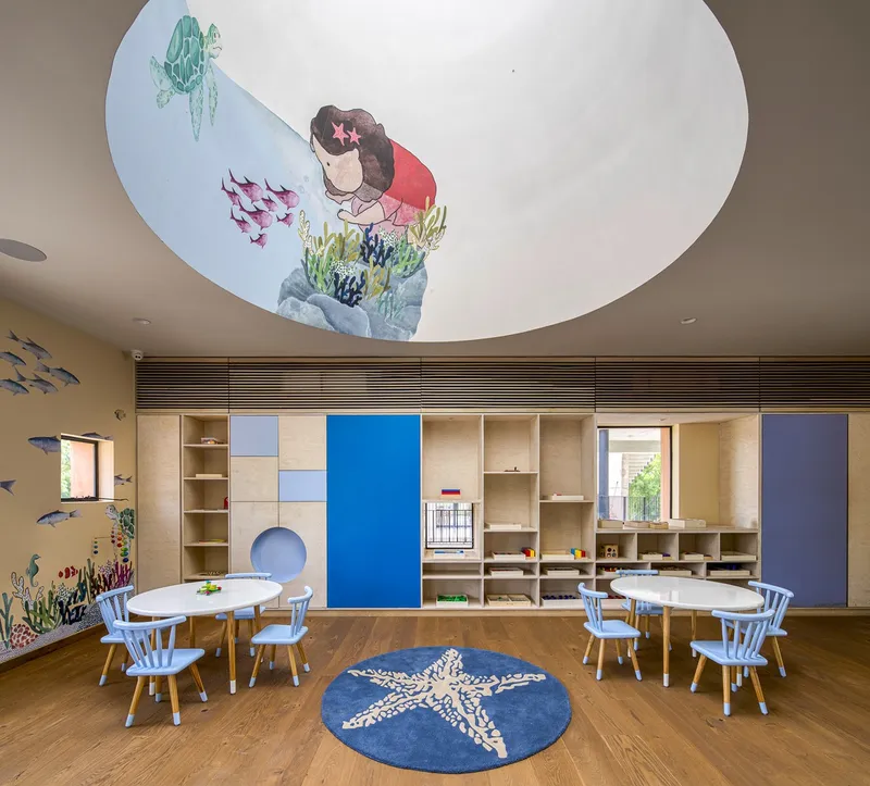 Classroom with painted ceiling mural depicting underwater scene above modular plywood storage wall and round carpet