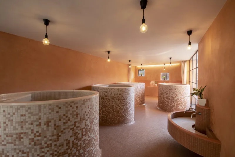 Bathroom interior with curved mosaic tile partitions, peachy plaster walls and pendant bulb lighting