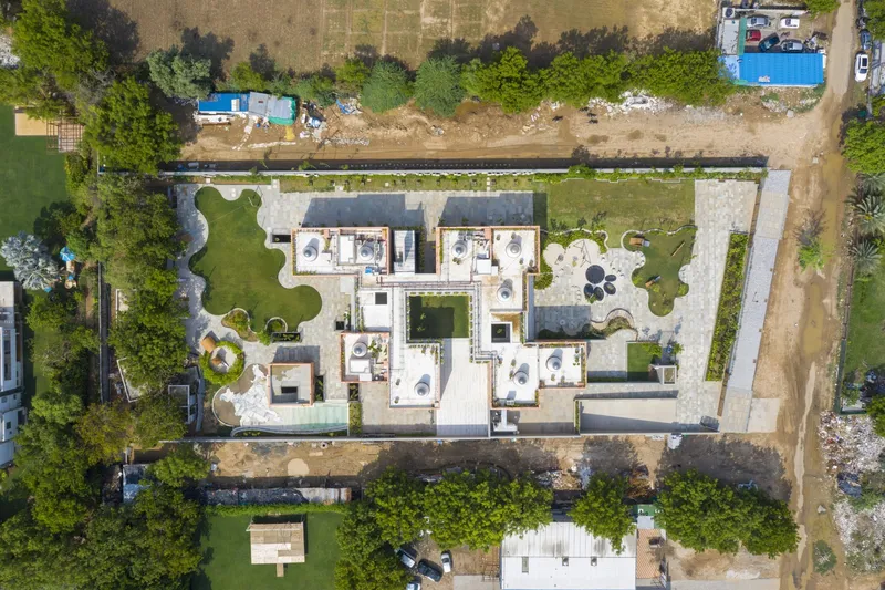 Aerial view of clustered flat-roofed volumes with skylights arranged around central courtyards flanked by trees and construction debris