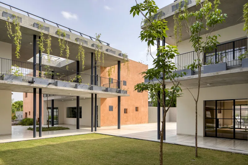 Courtyard view showing upper level balconies with hanging plants and young trees in lawn below