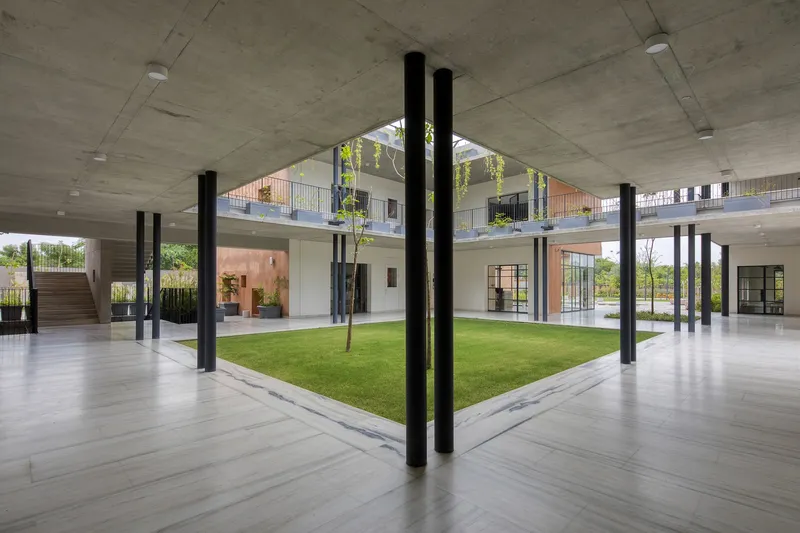 Covered ground floor with black steel columns framing a central courtyard with grass and young trees