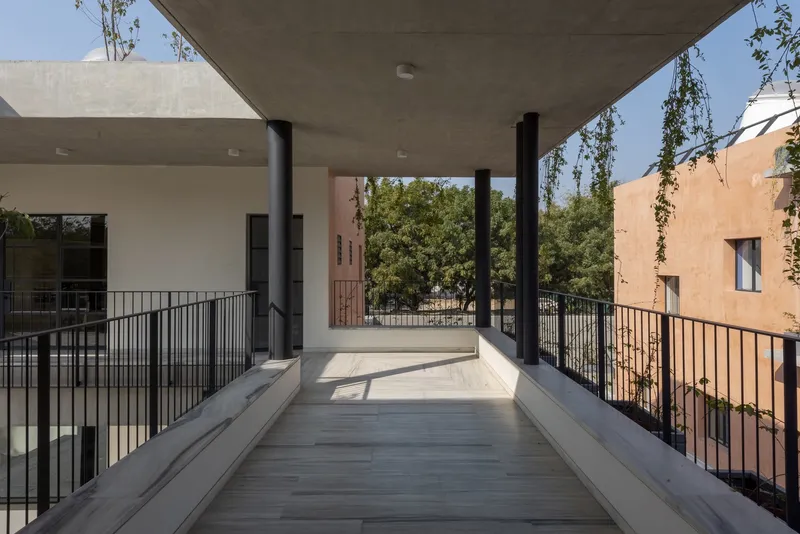 Elevated concrete walkway with steel railings connecting two building volumes under a clear sky