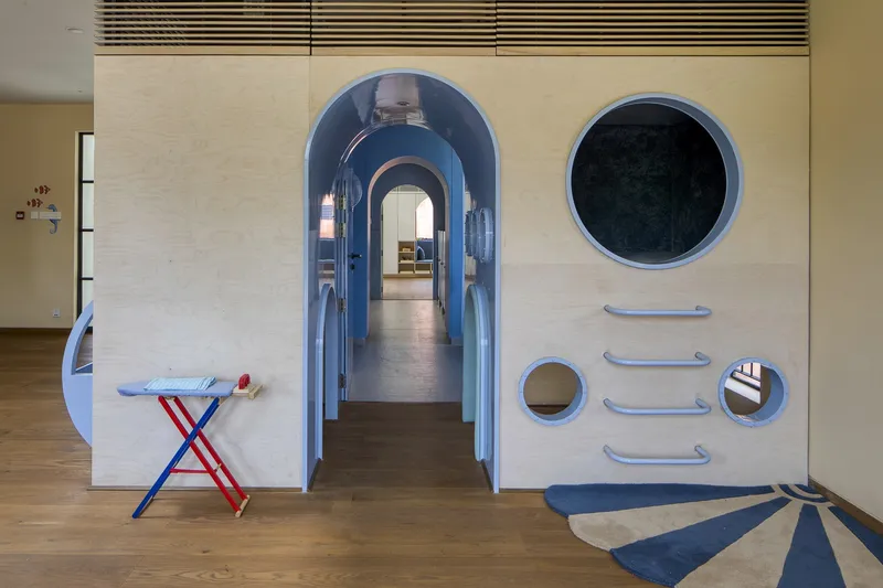 Arched blue corridor portal with circular and horizontal bar details on a plywood panel facade