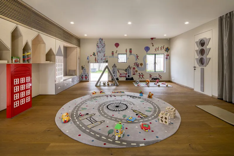 Play area with house-shaped storage niches, circular floor mat and wall decals under recessed ceiling lights
