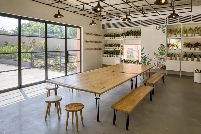 Timber dining table with benches and stools beneath black steel pendant lights and potted plant shelves