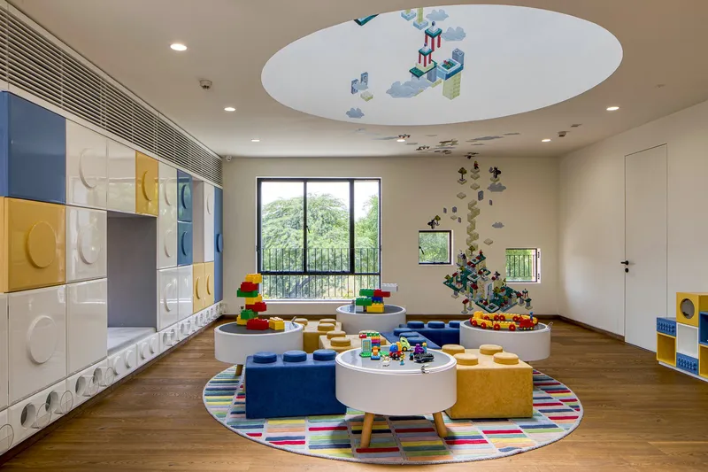 Playroom with circular ceiling mural, tactile wall panels and central round tables surrounded by cushioned seating