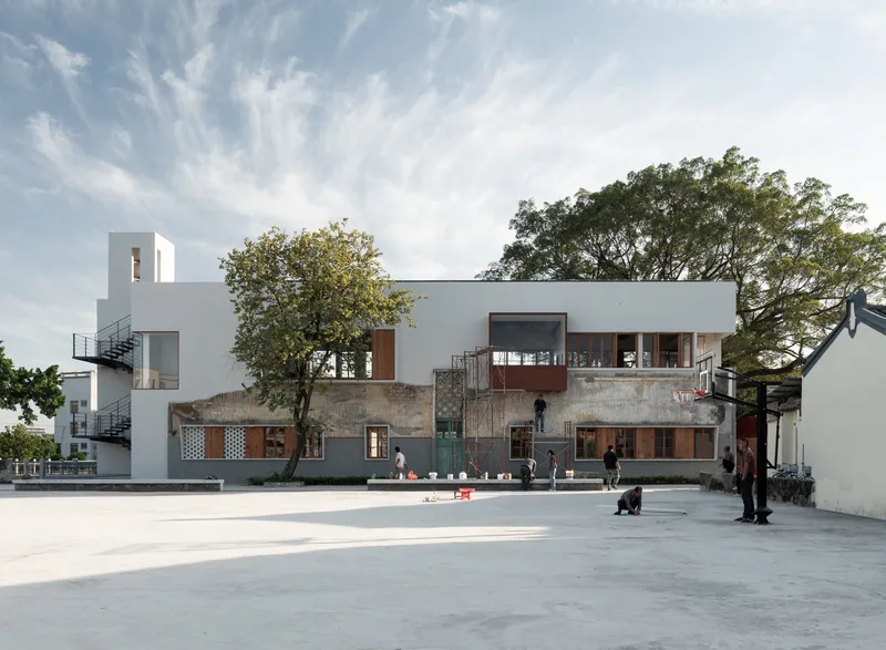 Street view of the mixed-material facade with white volumes, weathered concrete, and preserved trees