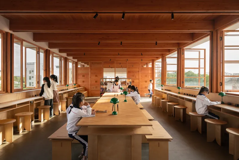 Reading room with exposed timber ceiling, long communal tables, and windows on both sides