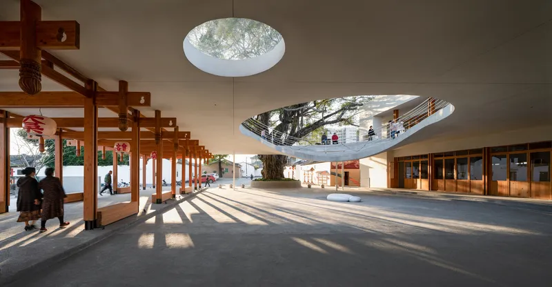 Interior plaza with timber colonnade and circular skylight reflecting a tree from above