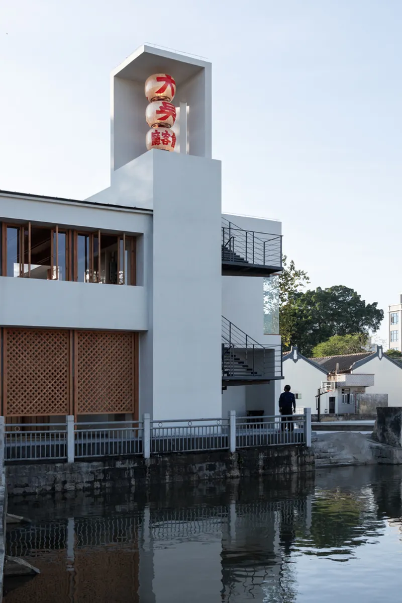 White tower with recessed signage box above lattice screens and metal stairs reflected in the canal below