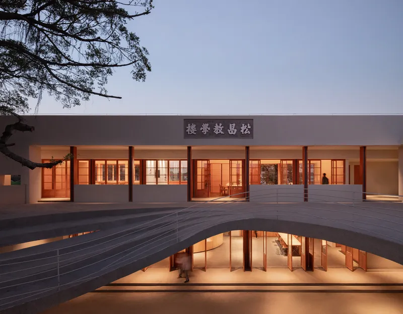 Courtyard elevation at dusk with illuminated timber-framed windows and a curved platform over a sunken level