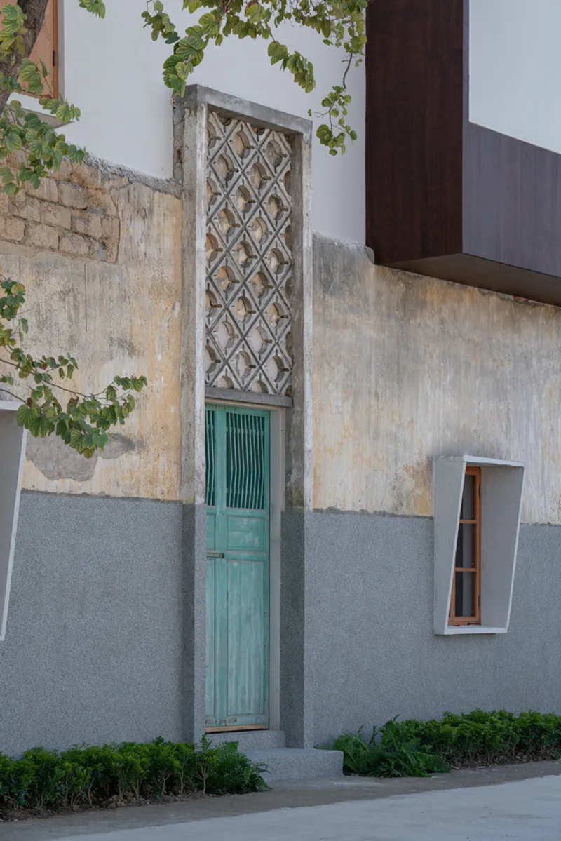 Narrow turquoise door with lattice transom set in a weathered two-tone plaster wall with greenery above