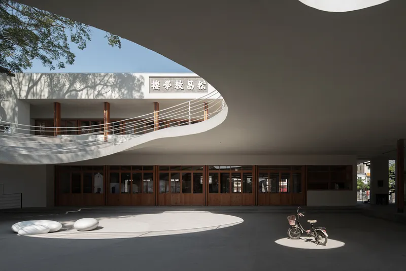 View of the courtyard showing timber framed glazing beneath the curved canopy with a bicycle in sunlight