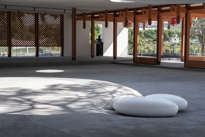 Interior space with timber columns and lattice screens casting dappled shadows across the grey floor