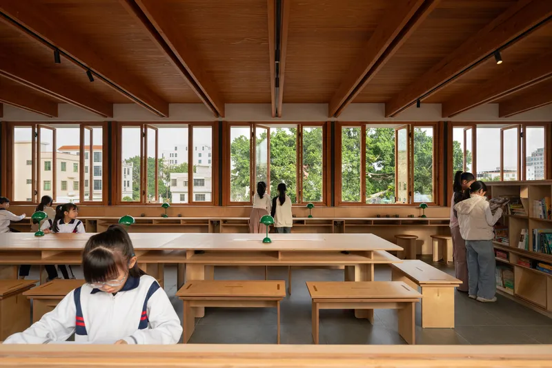 Library reading room with exposed timber beams and ceiling, full-height windows, and students at wooden desks