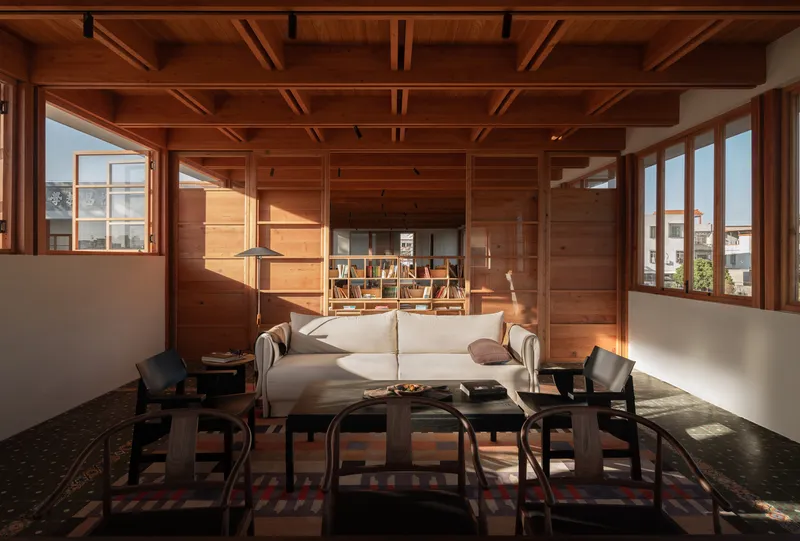 Interior lounge with timber-framed ceiling, low seating around a coffee table, and afternoon sunlight streaming through windows