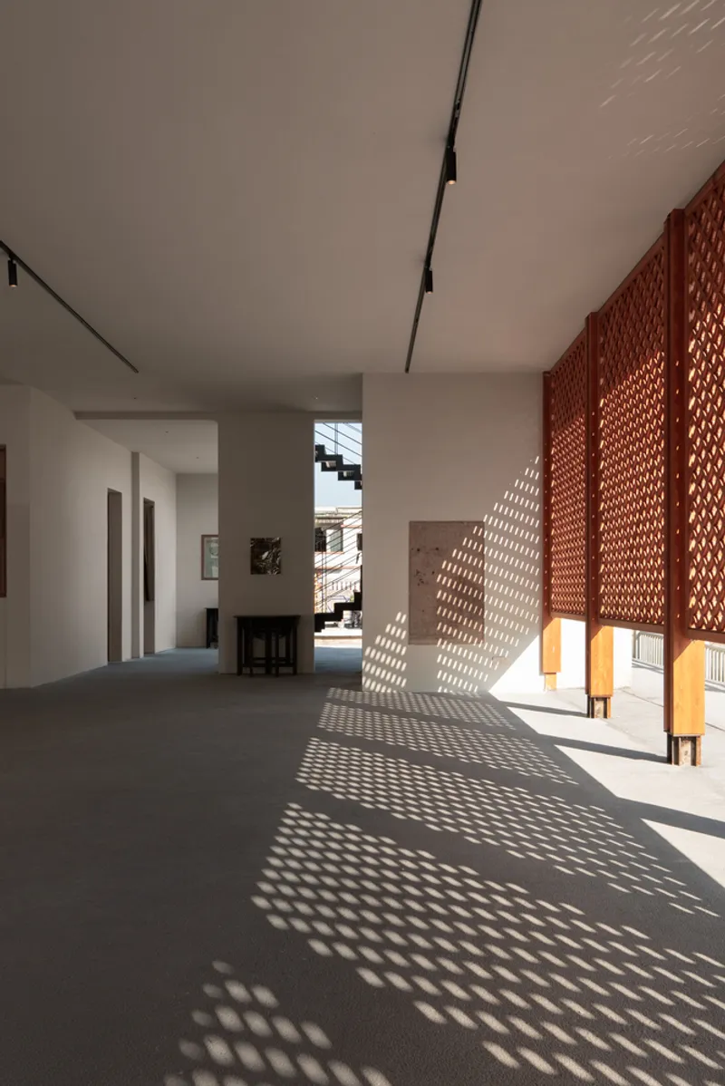 Interior corridor with perforated timber screens filtering sunlight into geometric shadow patterns on grey flooring