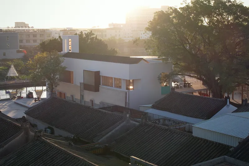 Aerial view of the white rendered volumes and vertical tower element among traditional rooftops in morning haze