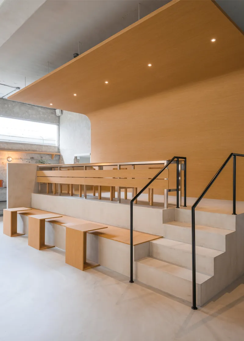 Raised platform: birch plywood stepped seating with integrated tables, black steel railing, timber ceiling panel above