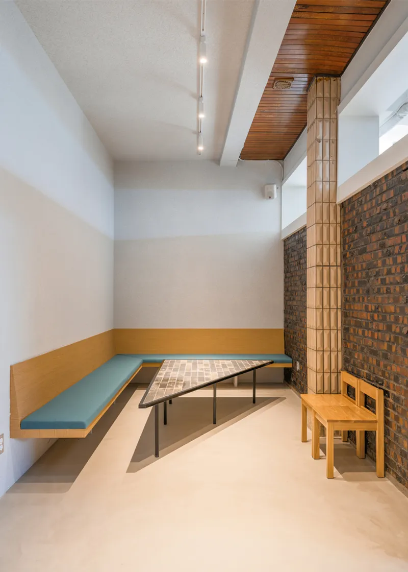 Alcove: blue upholstered bench, slim timber table, exposed stone and brick wall, timber column, timber slat ceiling above