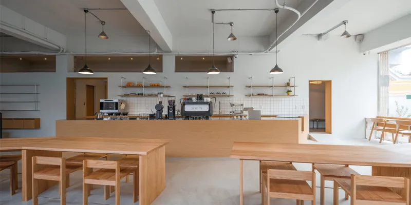 From behind the bar: birch communal tables, timber stools, white walls, pendant lamps, clerestory windows, winter light