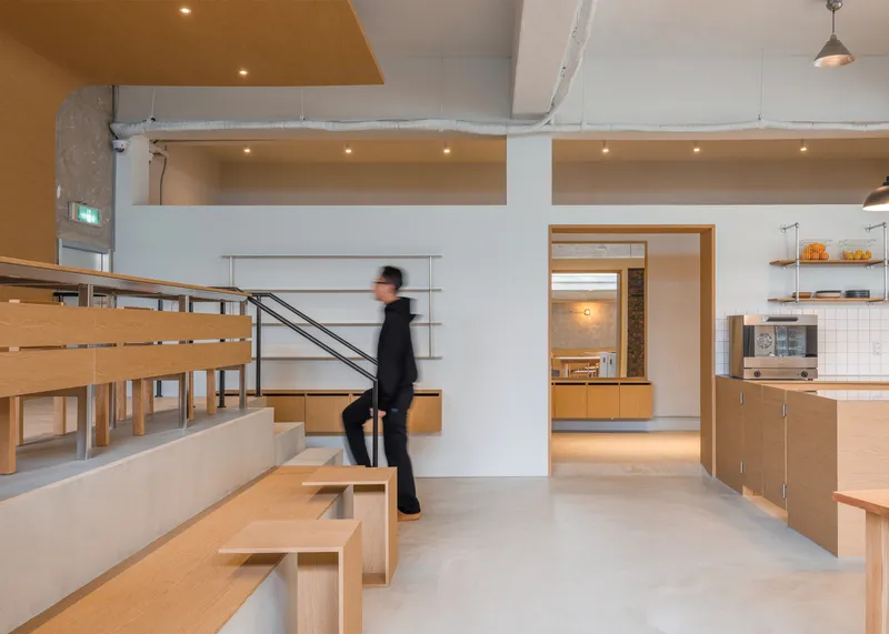 Circulation: figure descending the stair beside the raised platform, birch plywood benches, timber ceiling panel, bar beyond