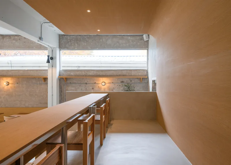 Upper platform intimate: birch plywood desk along the wall, timber ceiling, clerestory strip window, exposed concrete above, warm sconces