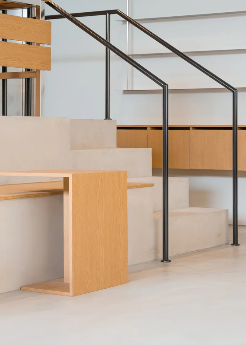 Stair detail: black steel railing meeting birch plywood bench and step, clean junction
