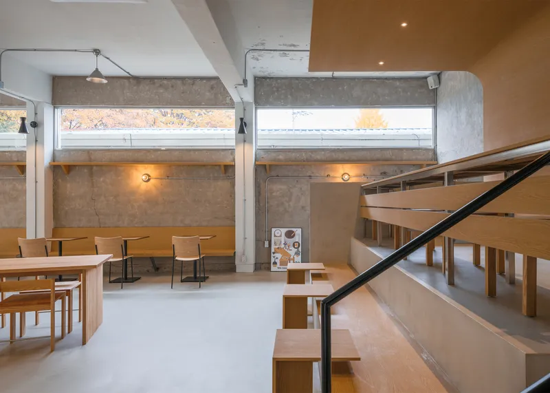 Platform and stair from below: black steel railing, birch benches, timber ceiling panel, exposed concrete walls, clerestory light