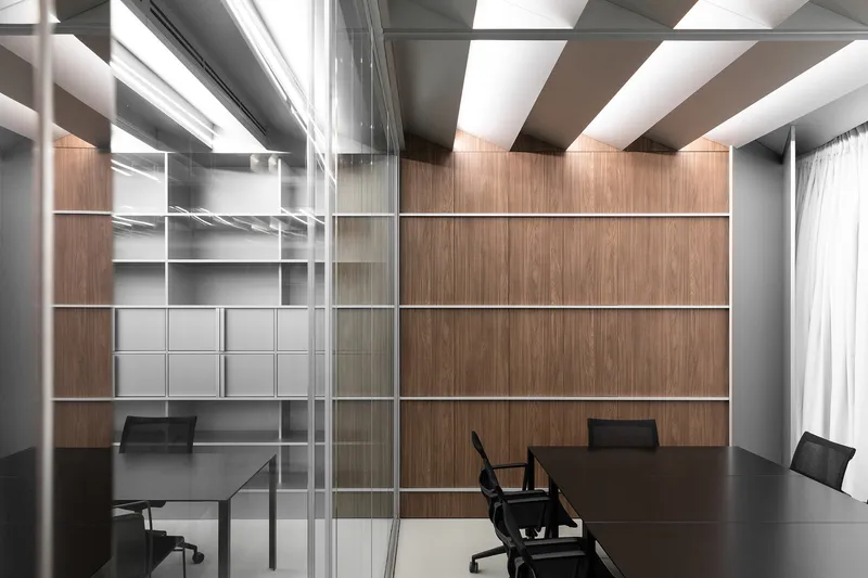 Private office through glass: walnut wall, grey open shelving unit, black desk, ceiling baffles above