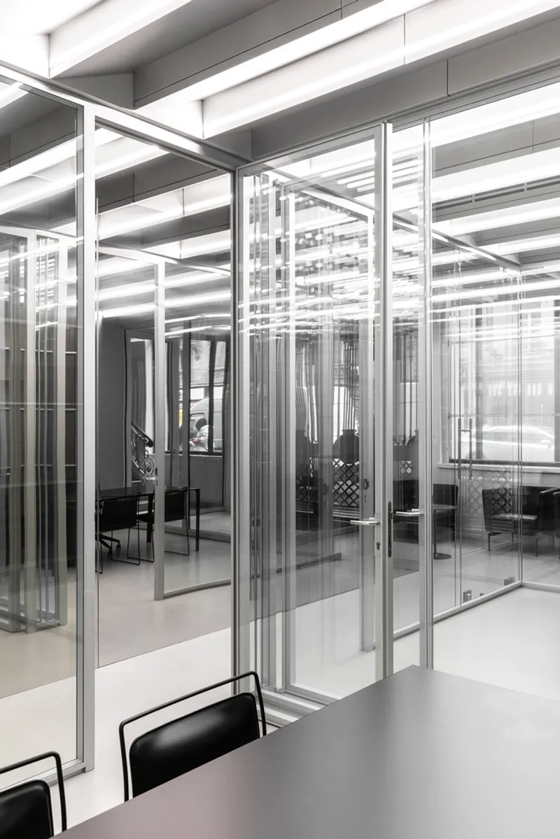 Glass partitions: multiple layers reflecting and overlapping, steel frames, meeting chairs visible through