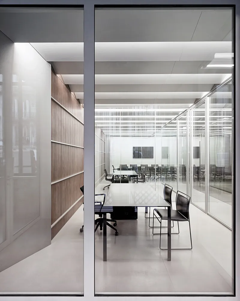 Through floor-to-ceiling glass: meeting room interior with walnut wall, open shelving, black furniture