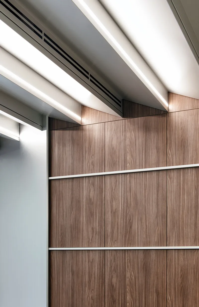 Wall junction: walnut timber panels meeting white ceiling baffles, aluminium trim at the edge