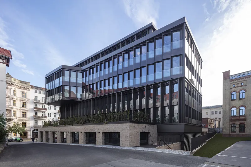 Street view of the gridded glass facade rising above a brick base under afternoon clouds