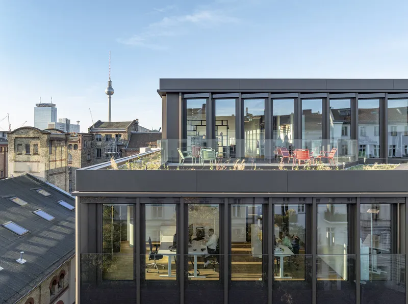 Stacked office floors with full-height glazing and planted roof terrace overlooking the city skyline